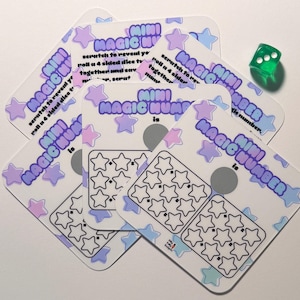 May include: Several Mini Magic Number scratch cards with a pastel star design. The cards feature a scratch-off area and star illustrations. A green die is positioned nearby, adding a playful element.
