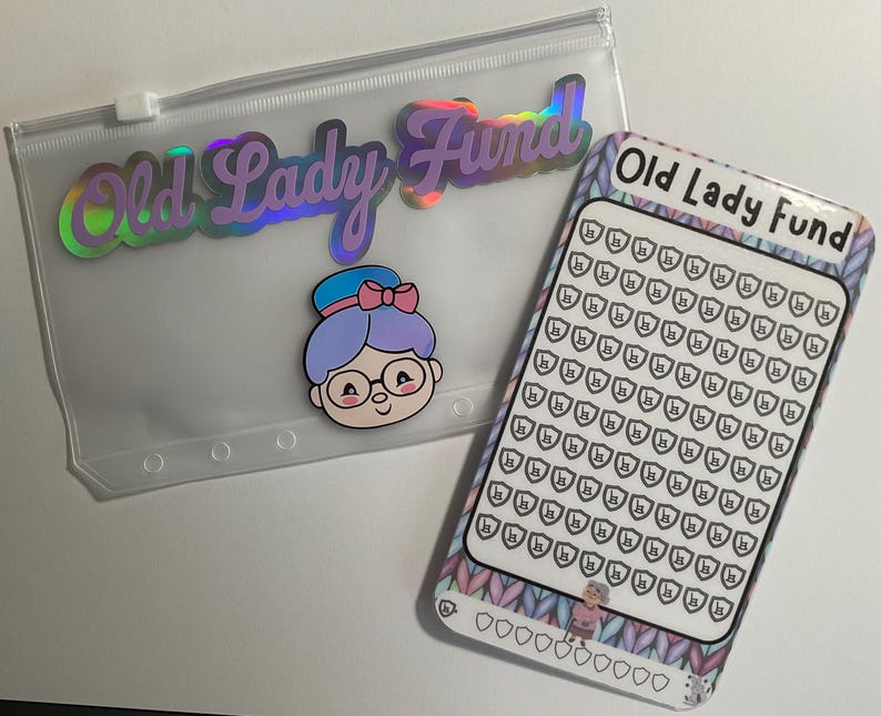 K&ouml;nnte beinhalten: Eine transparente Rei&szlig;verschlusstasche und ein Spar-Tracker mit dem Text "Old Lady Fund". Die Tasche hat ein holografisches Etikett und einen Cartoon einer Frau mit Brille. Der Spar-Tracker hat einen gemusterten Rand und ein Raster aus Schilden.