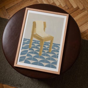 Top-down angled portrait frame mockup: light oak wood frame styled on a round dark brown leather ottoman over a textured neutral rug and parquet hardwood floor, cozy Scandinavian/minimal home-decor staging with natural light — ideal mockup for wall art prints, gallery wall, printable poster listings.