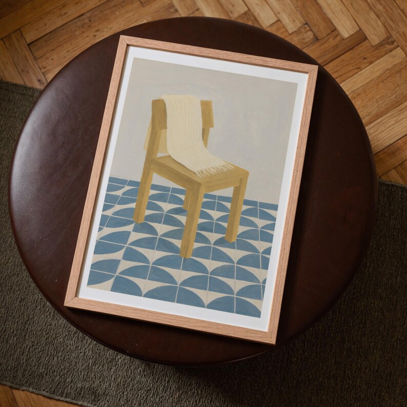 Top-down angled portrait frame mockup: light oak wood frame styled on a round dark brown leather ottoman over a textured neutral rug and parquet hardwood floor, cozy Scandinavian/minimal home-decor staging with natural light — ideal mockup for wall art prints, gallery wall, printable poster listings.