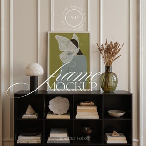Puede incluir: Un mueble de almacenamiento negro con múltiples estantes exhibe objetos decorativos. Una impresión enmarcada con un diseño de mariposa cuelga encima. También son visibles una lámpara, un jarrón con plantas secas, libros y cuencos. Las palabras "Frame Mockup" están escritas en la imagen.