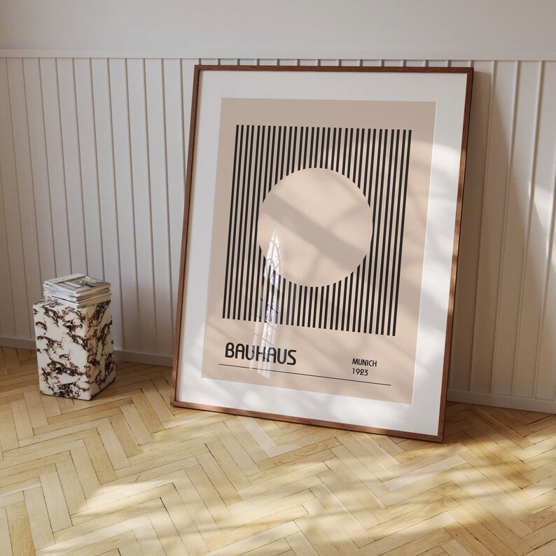 May include: A framed print with a black and white striped design and a large circle in the center. The circle is a light beige color. The print has the text "BAHAUS" in black letters and "MUNICH 1923" in smaller black letters.