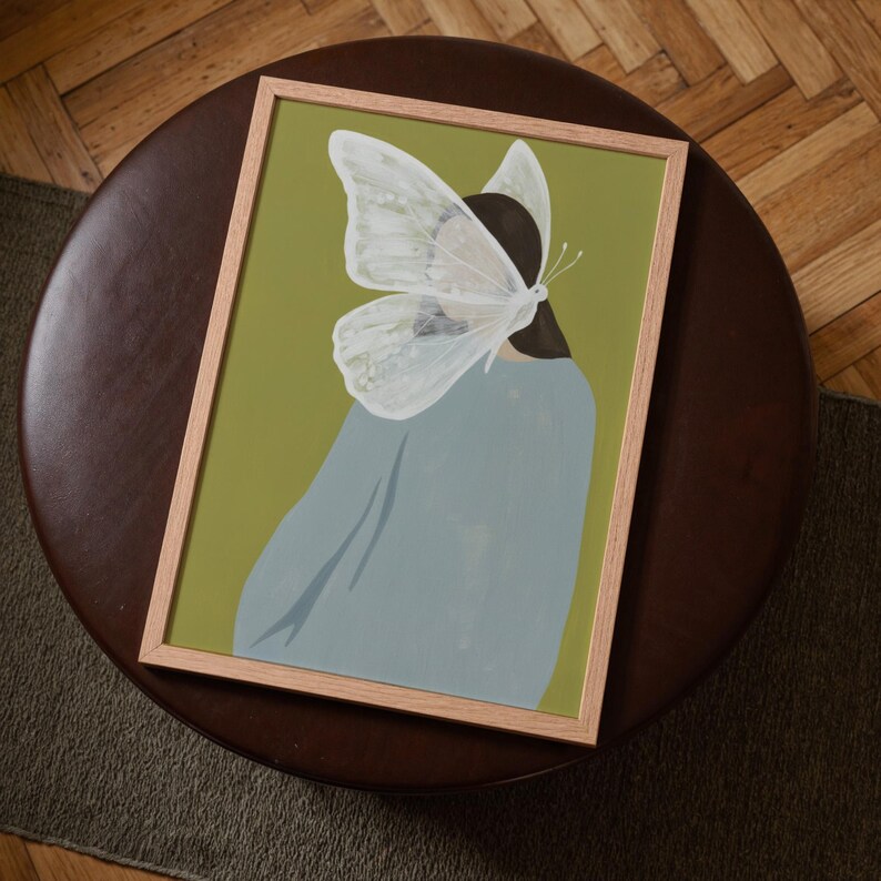 Top-down angled portrait frame mockup: light oak wood frame styled on a round dark brown leather ottoman over a textured neutral rug and parquet hardwood floor, cozy Scandinavian/minimal home-decor staging with natural light — ideal mockup for wall art prints, gallery wall, printable poster listings.