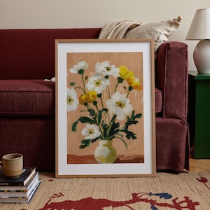 K&ouml;nnte beinhalten: Ein gerahmter Kunstdruck mit einem Blumenarrangement aus wei&szlig;en und gelben Blumen in einer gr&uuml;nen Vase. Das Kunstwerk hat einen neutralen Hintergrund und ist in einem hellen Holzrahmen ausgestellt. Der Druck befindet sich in der N&auml;he eines weinroten Sofas und eines gemusterten Teppichs.