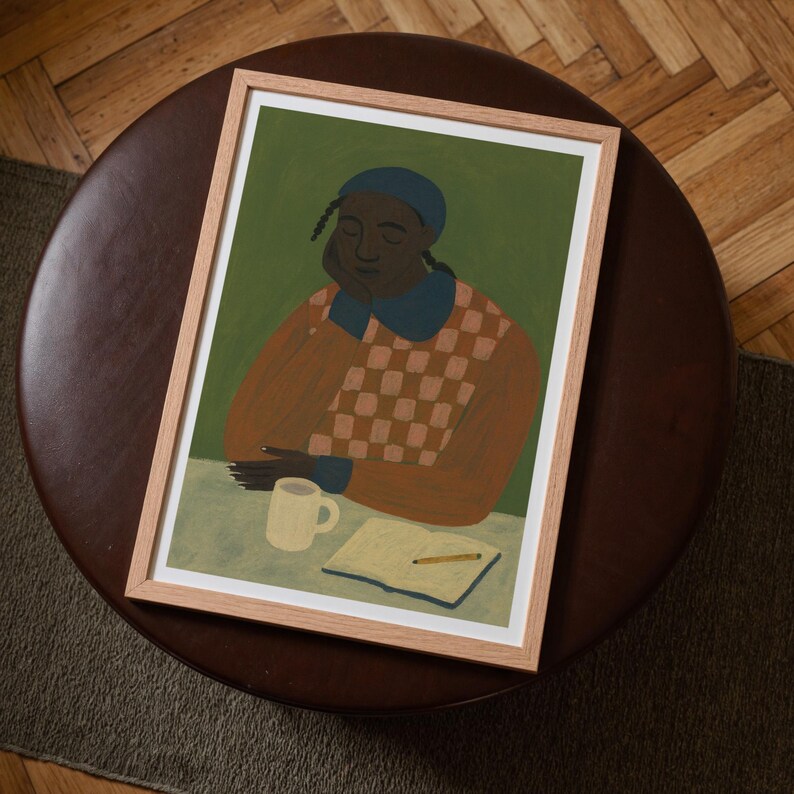 Top-down angled portrait frame mockup: light oak wood frame styled on a round dark brown leather ottoman over a textured neutral rug and parquet hardwood floor, cozy Scandinavian/minimal home-decor staging with natural light — ideal mockup for wall art prints, gallery wall, printable poster listings.