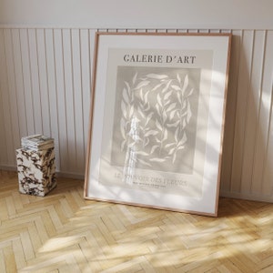 May include: A framed print with a beige background and white floral design. The text "GALERIE D'ART" and "LE POUVOIR DES FLEURS" is printed on the print.
