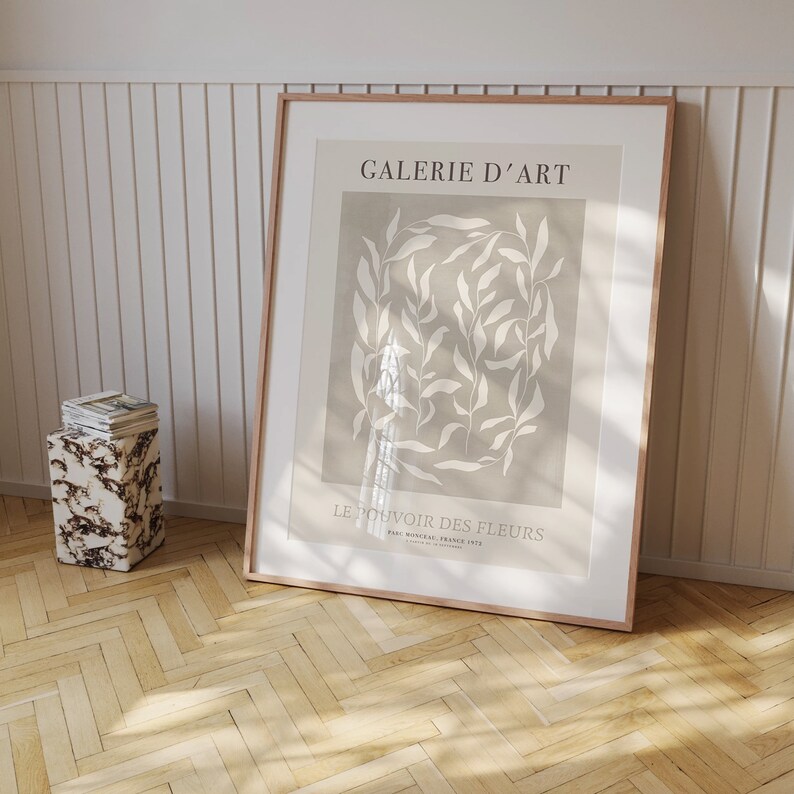 May include: A framed print with a beige background and white floral design. The text "GALERIE D'ART" and "LE POUVOIR DES FLEURS" is printed on the print.