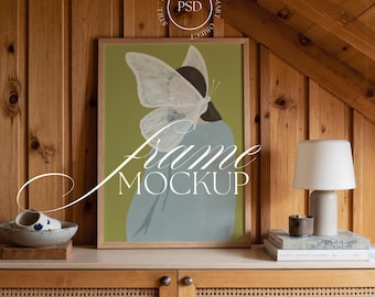 May include: A framed art print featuring a butterfly design with a woman's silhouette in a light blue dress. The artwork is displayed on a wooden cabinet with a lamp, books, and a decorative bowl. The words "Frame Mockup" are written on the artwork.