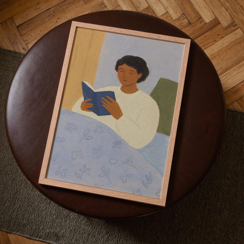 Top-down angled portrait frame mockup: light oak wood frame styled on a round dark brown leather ottoman over a textured neutral rug and parquet hardwood floor, cozy Scandinavian/minimal home-decor staging with natural light — ideal mockup for wall art prints, gallery wall, printable poster listings.