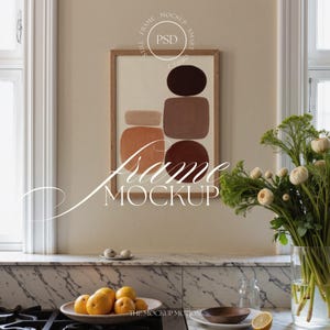 Puede incluir: Una impresión artística abstracta enmarcada con formas marrones y naranjas cuelga sobre una encimera. El marco es de madera. El texto "Frame Mockup" se muestra en cursiva. Un cuenco de naranjas y un jarrón de flores están en la encimera.