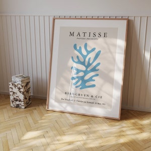 May include: A framed poster with a blue abstract design by Henri Matisse. The poster is titled "Matisse Papiers D&eacute;coup&eacute;s" and features the text "Berggruen & Cie" and "Du Vendredi 27 F&eacute;vrier au Samedi 28 Mars 1953".