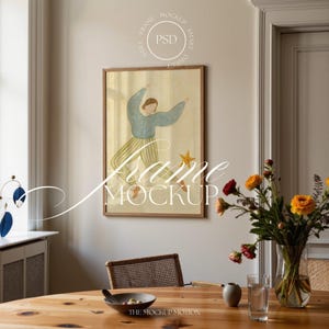 Op de afbeelding: Een ingelijst kunstwerk met een figuur in een blauwe top en gestreepte broek, met een ster, tegen een gele achtergrond. Het kunstwerk bevindt zich in een houten lijst. Een vaas met bloemen en een houten tafel staan op de voorgrond.