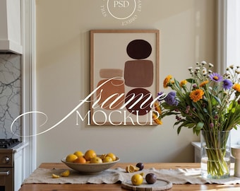 May include: A framed artwork with abstract shapes in brown and beige tones hangs above a wooden table. A bowl of fruit and a vase of colorful flowers are on the table. The text "Frame Mockup" is displayed.