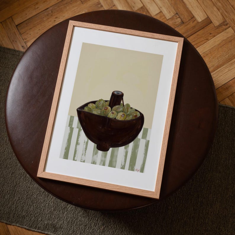 Top-down angled portrait frame mockup: light oak wood frame styled on a round dark brown leather ottoman over a textured neutral rug and parquet hardwood floor, cozy Scandinavian/minimal home-decor staging with natural light — ideal mockup for wall art prints, gallery wall, printable poster listings.