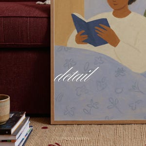 K&ouml;nnte beinhalten: Ein gerahmter Kunstdruck mit einer Person, die im Bett ein Buch liest. Das Kunstwerk hat eine weiche Farbpalette mit einer hellblauen, floral gemusterten Decke. Das Wort "detail" ist in wei&szlig;er Schrift auf dem Kunstwerk geschrieben.