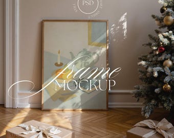 May include: A framed artwork with a still life painting featuring a teapot, candle, and fruit. The frame is leaning against a wall, with two wrapped gifts on the wooden floor. A Christmas tree with ornaments is in the background. The text "Frame Mockup" is overlaid on the image.