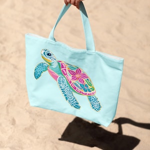 Op de afbeelding: Een lichtblauwe tote bag met een kleurrijk bloemenzee schildpad ontwerp. De tas heeft twee lange handvatten.