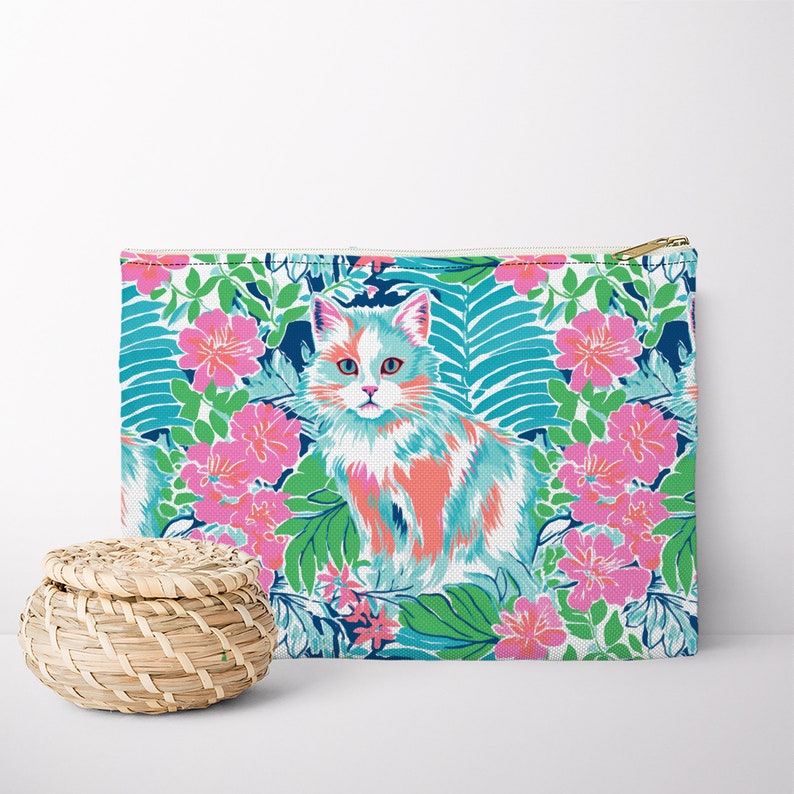 Pode incluir: Um gato branco, rosa e azul com estampa floral verde, azul e rosa sobre fundo branco. O gato est&aacute; sentado no centro da imagem. A estampa floral &eacute; um design tropical.