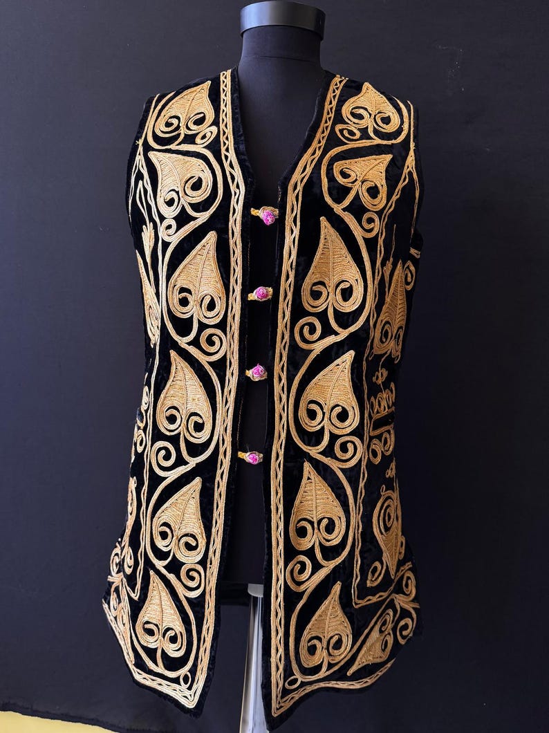 May include: Black velvet vest with gold embroidered leaf and swirl pattern. The V-neck vest is fastened with three pink buttons. The garment is displayed on a black mannequin.