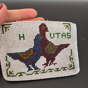 Pode incluir: Uma bolsa de moedas de contas brancas com um desenho de contas coloridas de dois pássaros. Os pássaros são vermelhos, azuis e dourados. As palavras "UTAH" e "HI" estão em contas verdes na bolsa.
