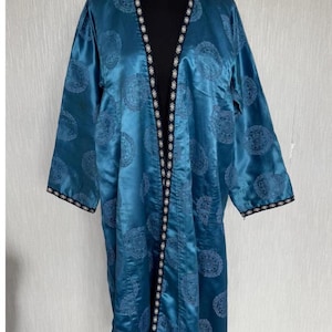 Könnte beinhalten: Eine tealblaue Satinrobe mit schwarzem und weißem Besatz. Die Robe hat ein Blumenmuster und einen langen, offenen Vorderteil.