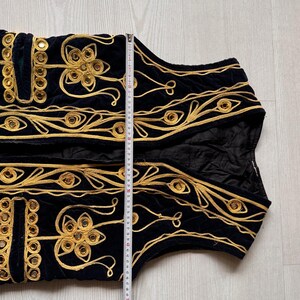 May include: Black velvet vest with gold embroidery and mirrored accents. The vest features intricate floral and geometric patterns. The length of the vest is approximately 20 inches.