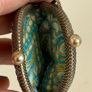 May include: A silver coin purse with a blue and gold floral pattern lining. The purse has a metal clasp with two silver knobs.