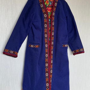 Könnte beinhalten: Ein langer, marineblauer Mantel mit einem Blumenfutter. Der Mantel hat einen V-Ausschnitt und ist mit einem bunten Stickmuster verziert.