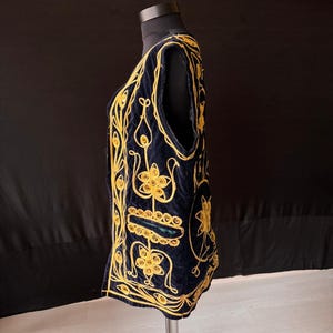 May include: A navy blue vest with intricate gold embroidery. The vest features a V-neck and a sleeveless design. The gold embroidery creates floral and geometric patterns across the front and sides of the vest. The vest is displayed on a mannequin.