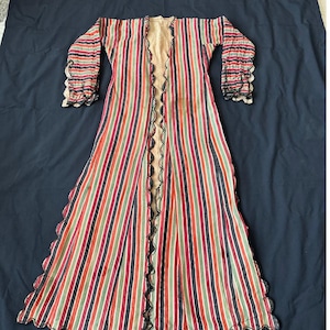 Op de afbeelding: Een lange, gestreepte robe met een gegolfde zoom en manchetten. De robe is gemaakt van een lichtgewicht stof en heeft een verscheidenheid aan kleuren, waaronder rood, groen, zwart en wit.