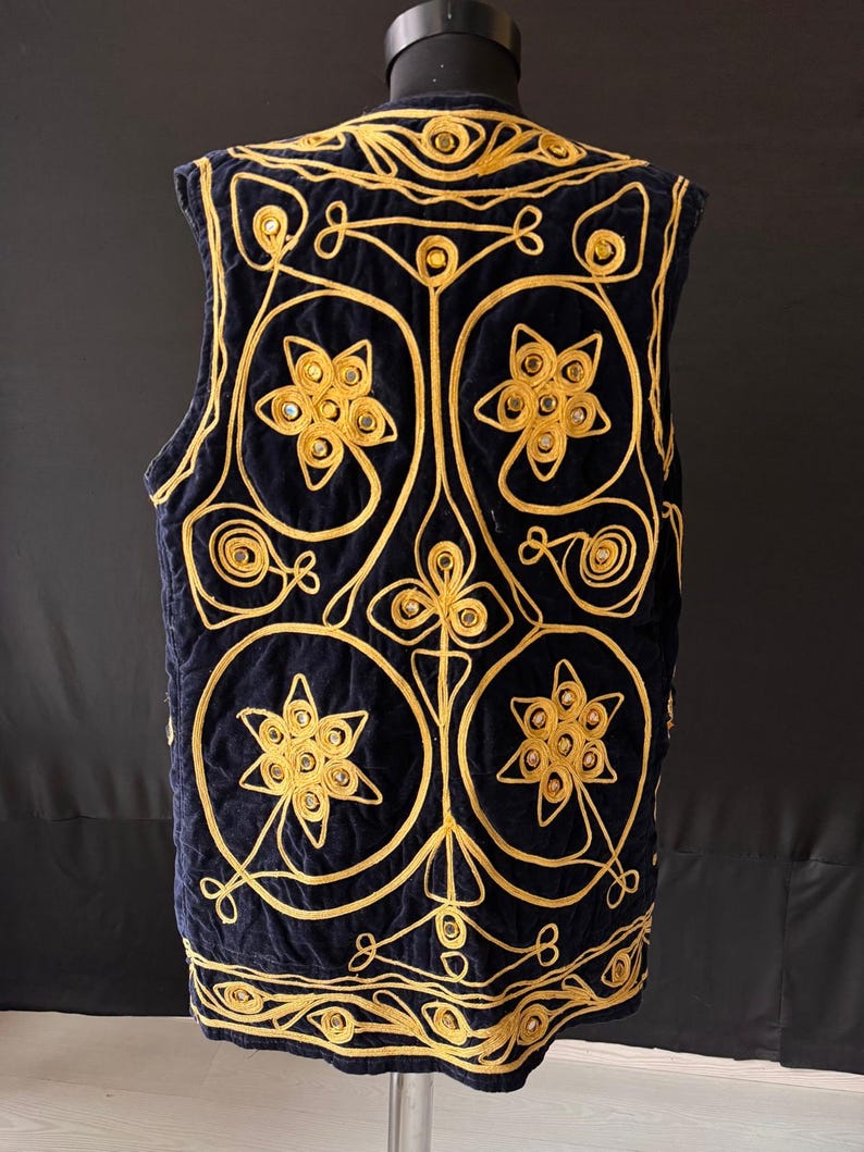 May include: A navy blue vest with intricate gold embroidery. The vest features a quilted design with floral and geometric patterns. The gold embroidery creates a striking contrast against the dark blue fabric, adding a touch of elegance and sophistication.