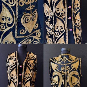May include: Black velvet vest with gold-coloured embroidered floral and scrollwork design. The vest features a V-neck, pink button closures, and a detailed pattern on the front and back. The vest is displayed on a mannequin.
