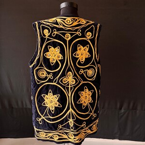 May include: A navy blue vest with intricate gold embroidery. The vest features a floral and geometric design, with circular and star-shaped elements. The gold embroidery stands out against the dark blue fabric, creating a striking contrast. The vest is displayed on a mannequin.