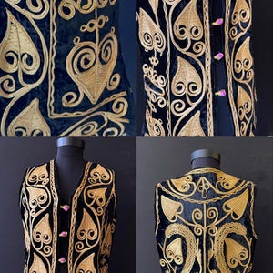 May include: Black velvet vest with gold-coloured embroidered floral and scrollwork design. The vest features a V-neck, pink button closures, and a detailed pattern on the front and back. The vest is displayed on a mannequin.