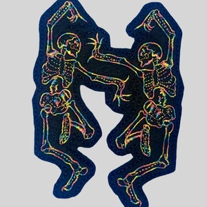 May include: Two skeletons dancing, outlined in rainbow iridescent thread on a black fabric patch.