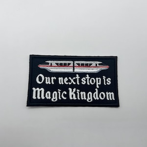 May include: Embroidered patch with a black background featuring a monorail design in white and red. The text "Our next stop is Magic Kingdom" is in white script. Ideal for Disney fans.