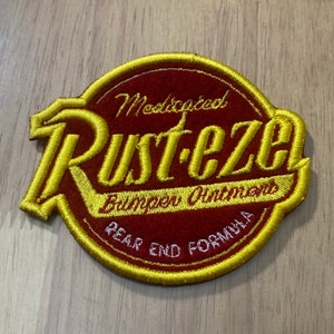 May include: A gold embroidered patch with the words "Rust-eze" in a stylized font. The patch also says "Medicated Bumper Ointment Rear End Formula".
