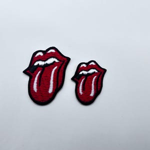 May include: Two embroidered patches featuring the iconic red tongue and lips design with white accents and a black border. One patch is larger than the other. The patches are likely for clothing or accessories.