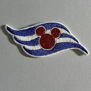May include: An embroidered patch featuring a stylized blue and white wavy flag design with a central red silhouette of a mouse head with two circular ears. The patch has a white border and is stitched with dense thread in a horizontal orientation.
