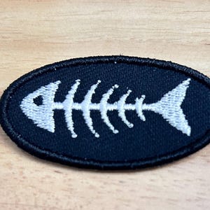 May include: White embroidered fish skeleton on a black oval patch.