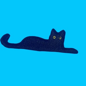 May include: A black cat with yellow eyes is lying down on a blue background.