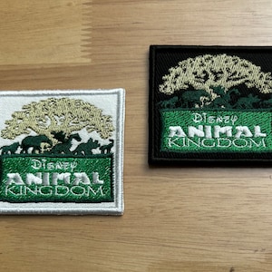 May include: Two embroidered patches featuring a green tree with animals and the text "Disney Animal Kingdom". One patch is white with green text and the other is black with white text.