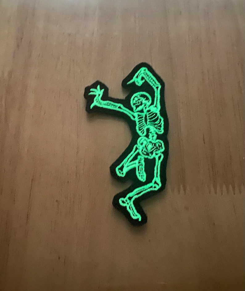 Puede incluir: Un parche negro con un esqueleto verde brillante en pose de baile. Los huesos del esqueleto est&aacute;n detallados con un color verde ne&oacute;n brillante, y el parche tiene un borde negro. Este parche es adecuado para temas de Halloween o g&oacute;ticos.