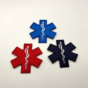May include: Three embroidered Star of Life patches in blue, red, and navy blue. Each patch features a white staff with a serpent, a symbol of emergency medical services. The patches are on a white background.