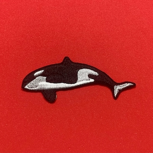 May include: Black and white embroidered patch of an orca whale on a red background.