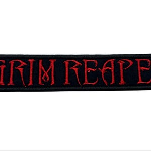May include: Black rectangular patch with the words "GRIM REAPER" embroidered in red thread. The text is in a stylized font. The patch has a black border and is set against a white background.