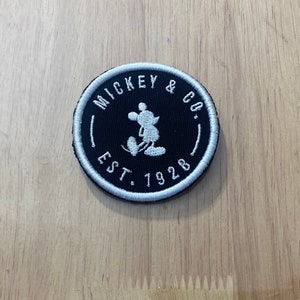 May include: A black and white embroidered patch with Mickey Mouse and the text "Mickey & Co. Est. 1928".