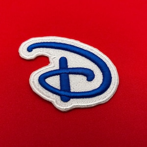 May include: Embroidered patch featuring the iconic blue and white Disney logo. The patch has a white border and a bright blue stylized letter "D" design. The patch is set against a vibrant red background.