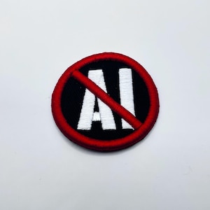 May include: Embroidered patch with a black background and a red border. The white letters "AI" are crossed out with a red diagonal line, indicating a prohibition. The patch is circular.