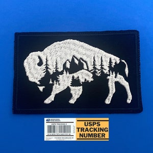 May include: White embroidered patch with a silhouette of a buffalo with a forest inside. The patch is on a black background. The text "USPS TRACKING NUMBER" is on a yellow label below the patch.